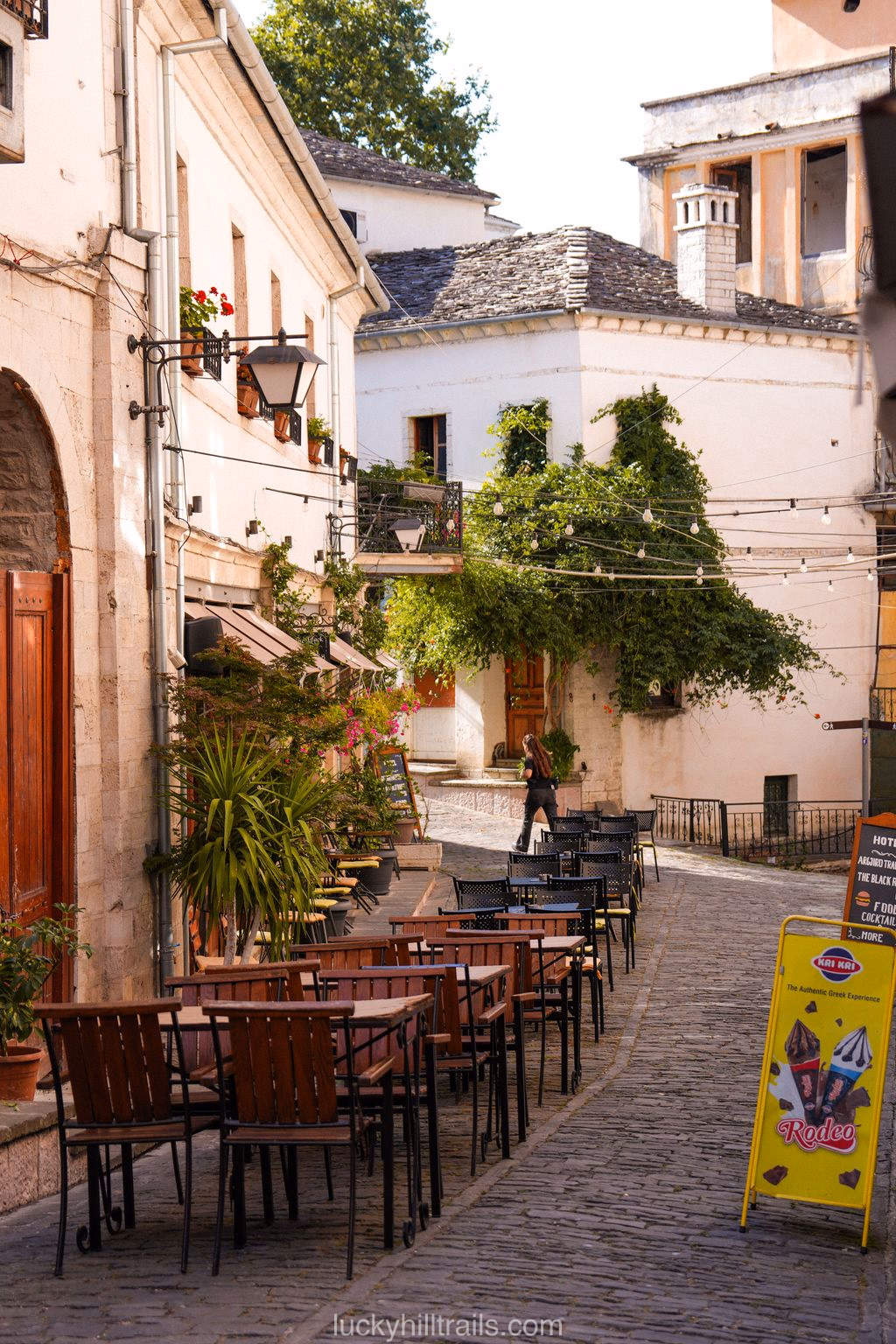 A cobblestone street in the old town of Gjirokastër with stone buildings and café tables