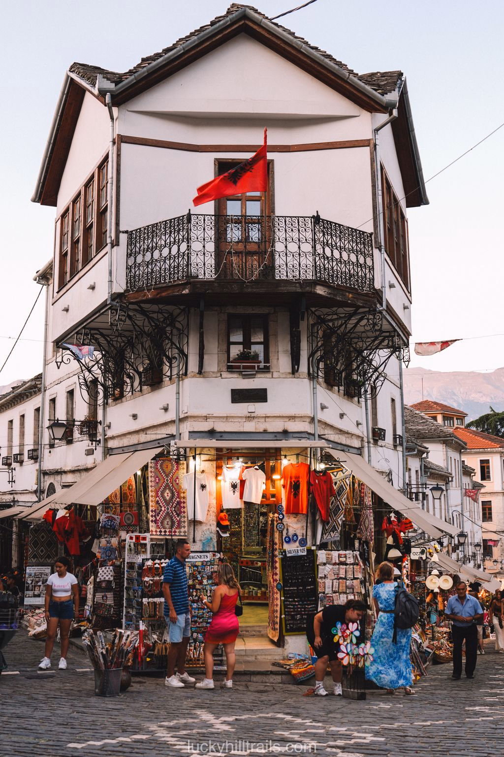 Traditional Ottoman building with a balcony and Albanian flag at the Gjirokastër bazaar — souvenir shops below