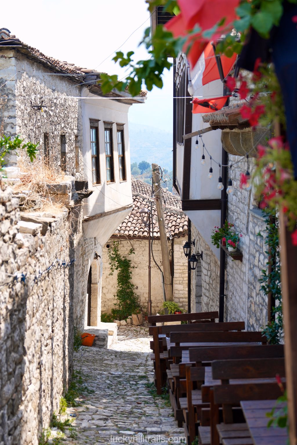 A narrow cobblestone street in old Berat with stone buildings and café tables outside