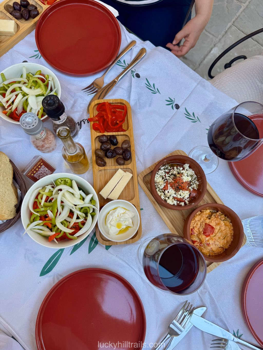 A table with traditional Albanian dishes: salads, dips, olives, cheese, and red wine at Amalia restaurant