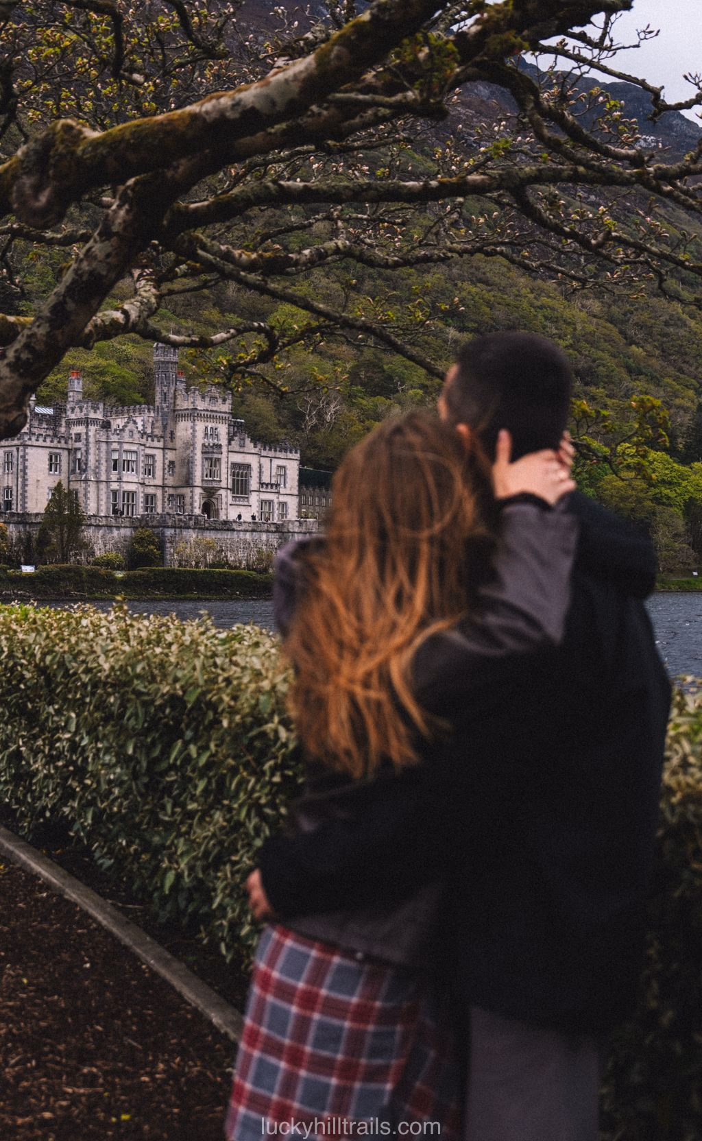 A couple admires Kylemore Abbey reflected in the lake, surrounded by the green hills of Connemara, Ireland