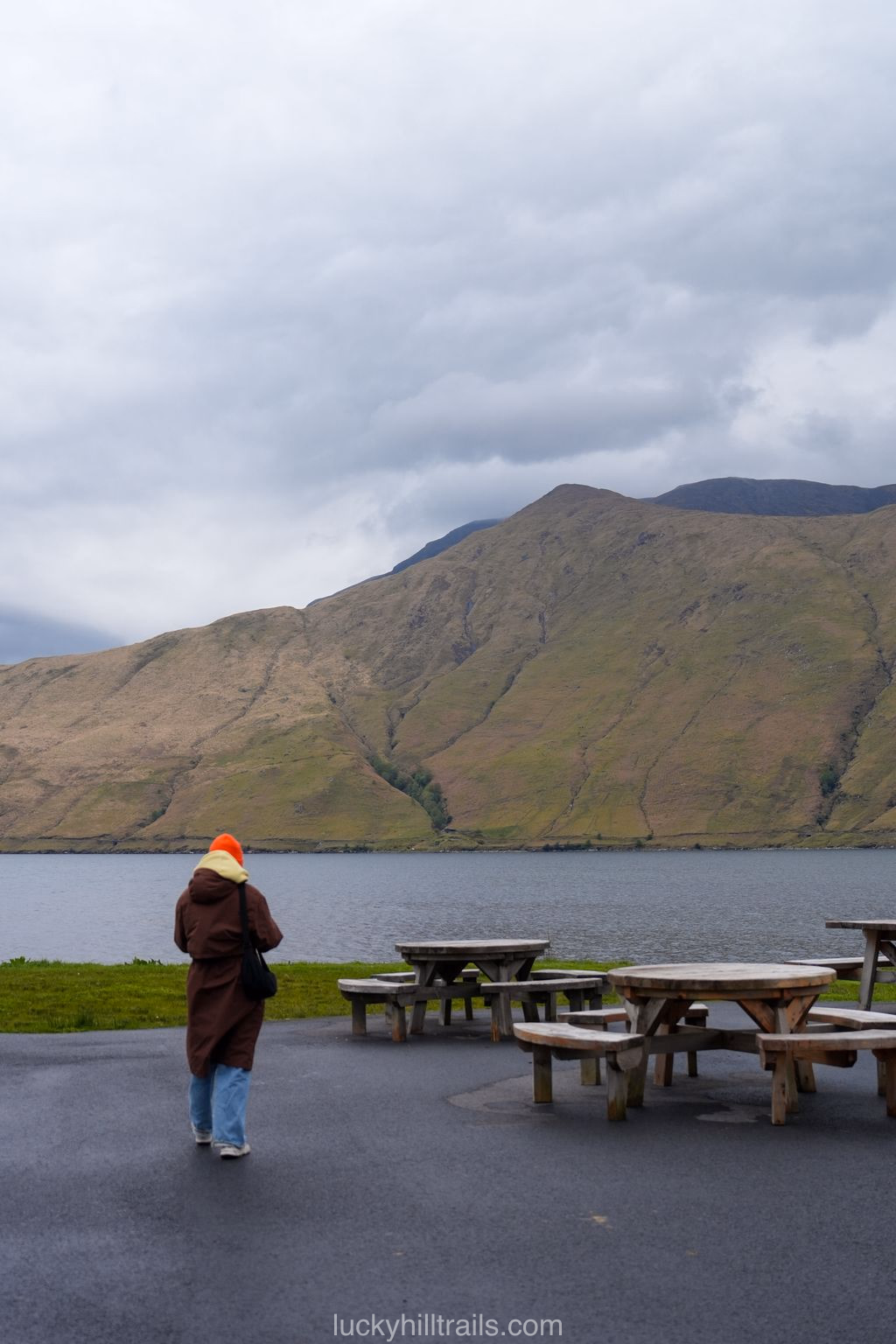 A visitor in an orange hat looks out over Killary Fjord and the mountains under an overcast sky, Connemara, Ireland