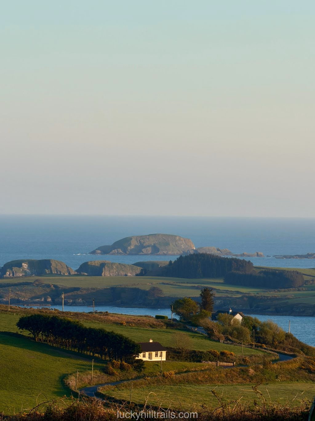 Panorama of the Irish coast with green fields, farmhouses and rocky islands in the ocean at sunset