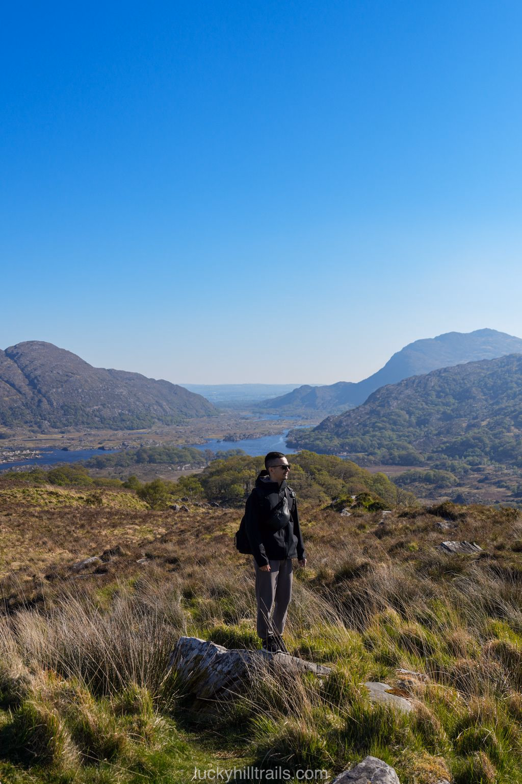 A hiker stands on rocks looking out over the valley with Killarney's lakes and mountains, Ladies' View, Ireland