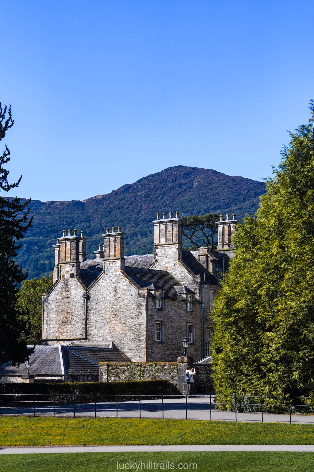 Victorian Muckross House mansion with stone towers against mountains and blue sky, Killarney, Ireland