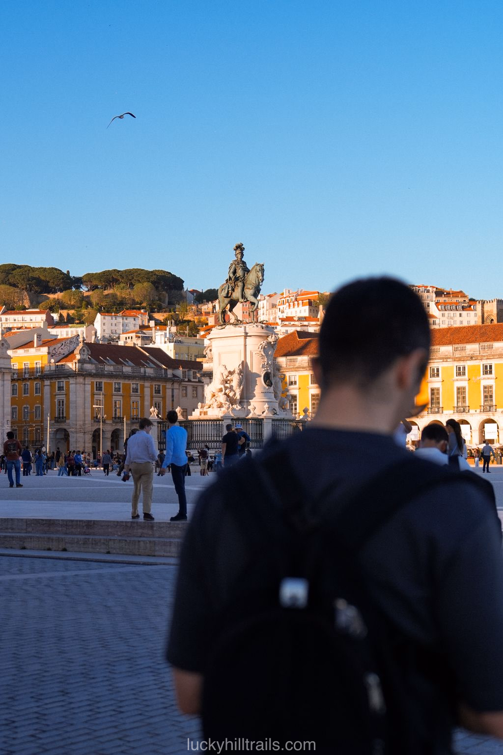 Man with backpack (back to camera) looking at the equestrian statue of King José I at Praça do Comércio, Lisbon, Portugal