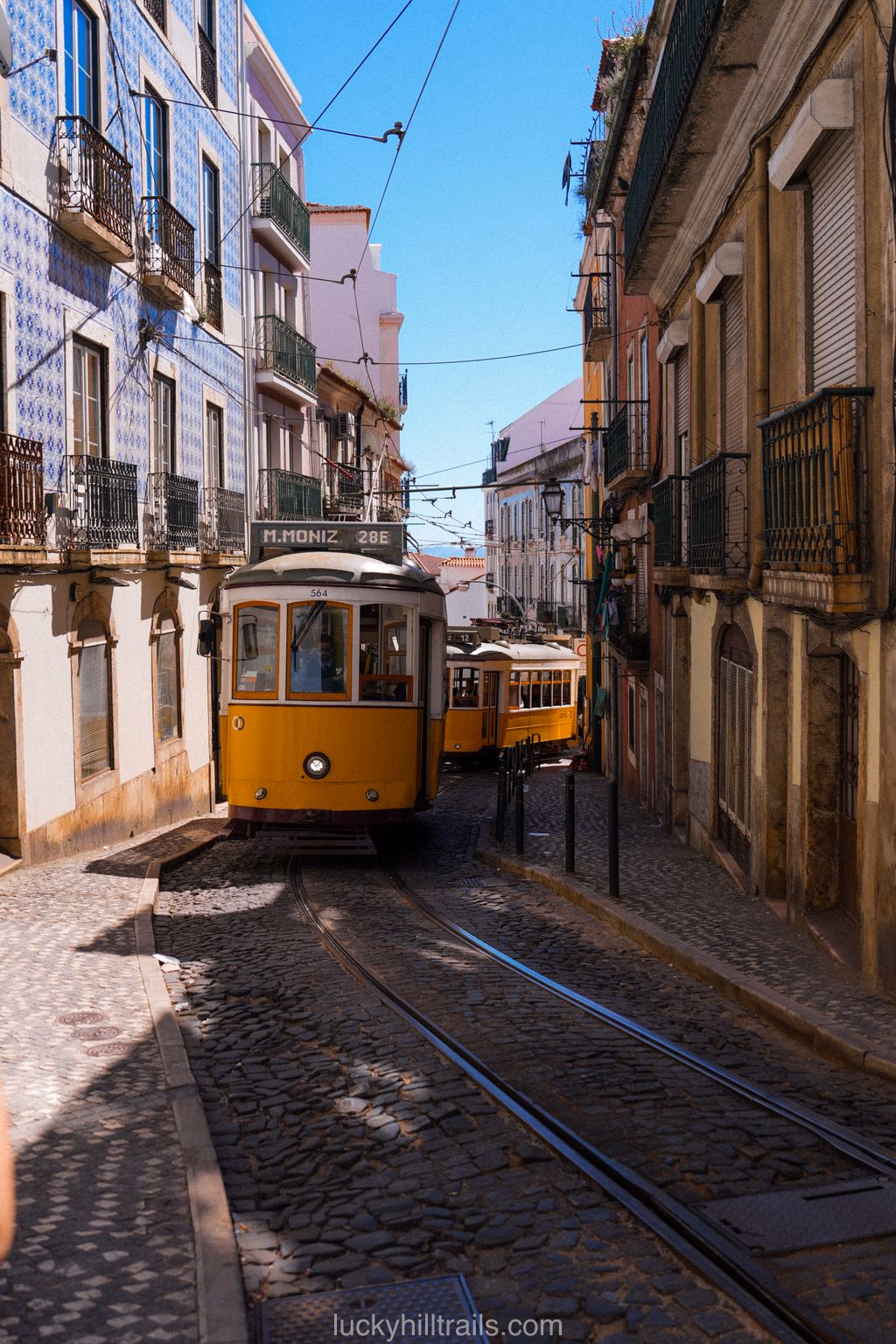 Two yellow Tram 28 cars on a narrow cobblestone street between azulejo-tiled buildings, Lisbon, Portugal