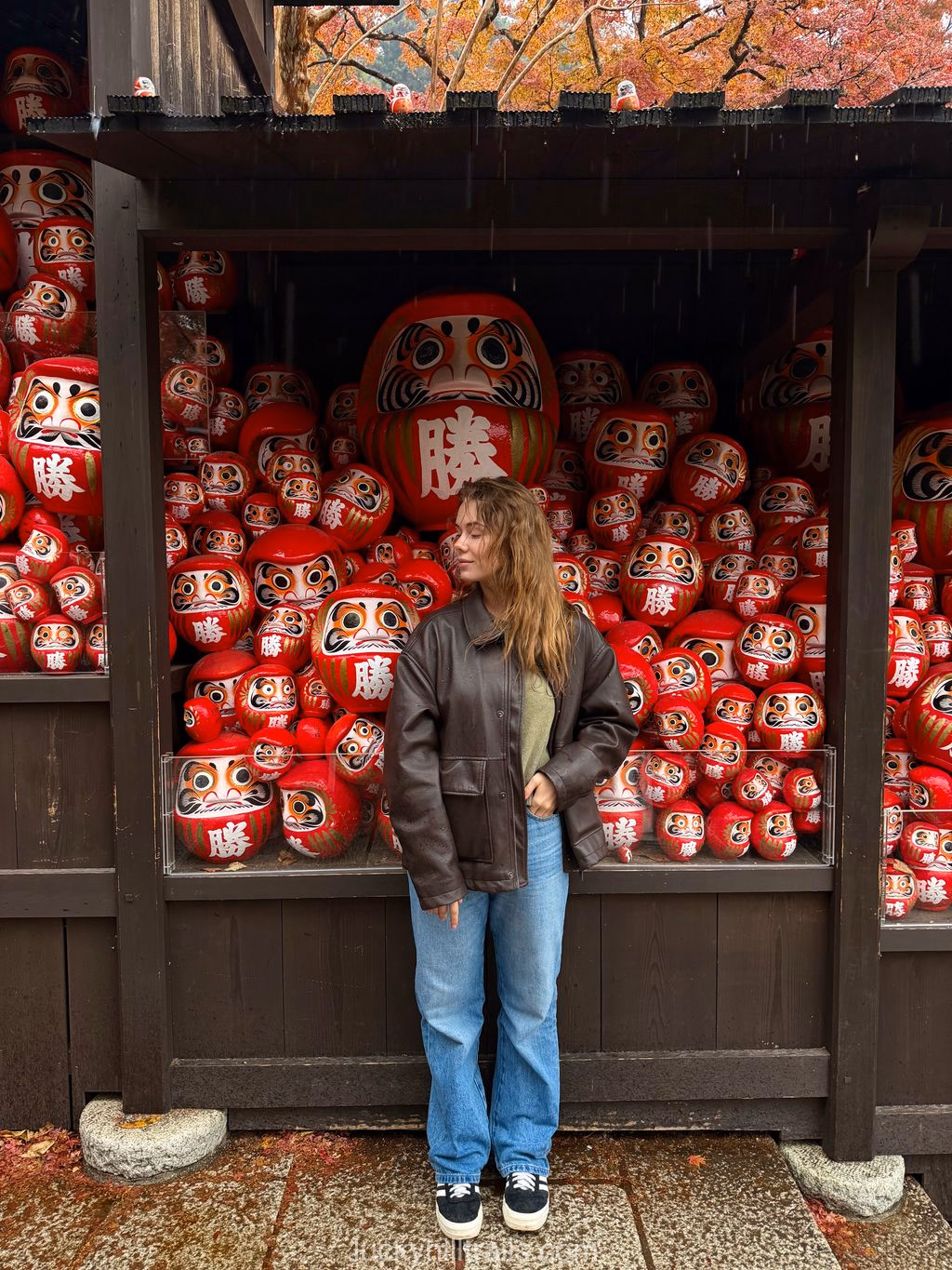 Girl standing in front of a display of red daruma dolls at Katsuo-ji Temple in autumn