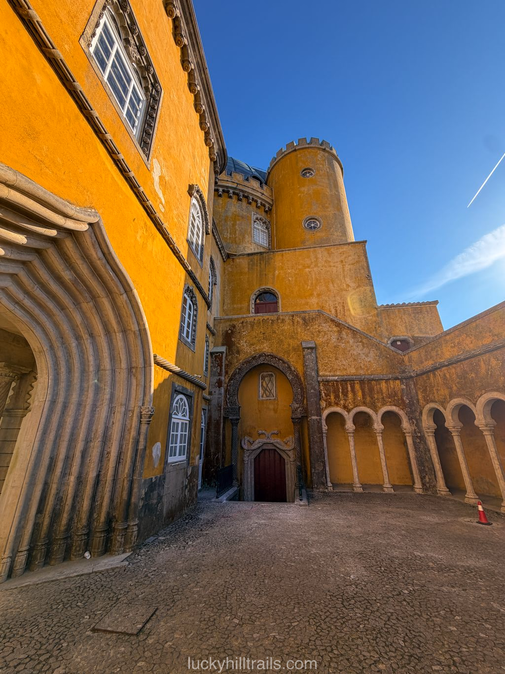 Low-angle view of the yellow walls and tower of Pena Palace with an arcade against a blue sky, Sintra, Portugal